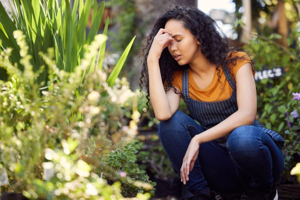 mujer rodeada de plantas cansada, con la mano en la cabeza y los ojos cerrados