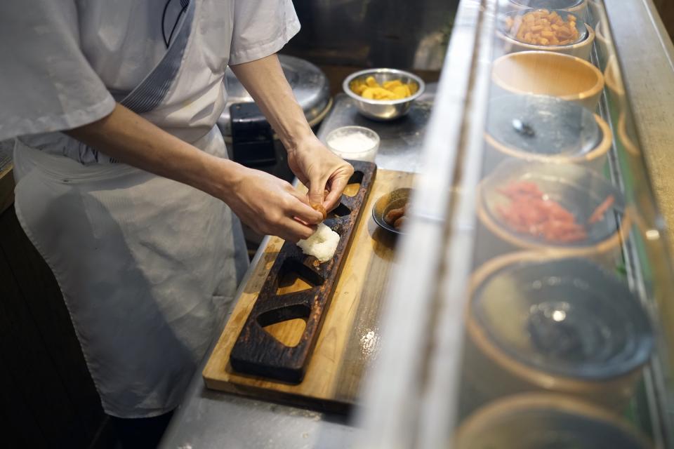 Yosuke Miura makes a rice ball with pieces of grilled salmon at Onigiri Asakusa Yadoroku, Tokyo's oldest onigiri restaurant, on June 3, 2024, in Tokyo. The word "onigiri" just became part of the Oxford English Dictionary this year. The humble sticky-rice ball, a mainstay of Japanese food, has entered the global lexicon. (AP Photo/Eugene Hoshiko)