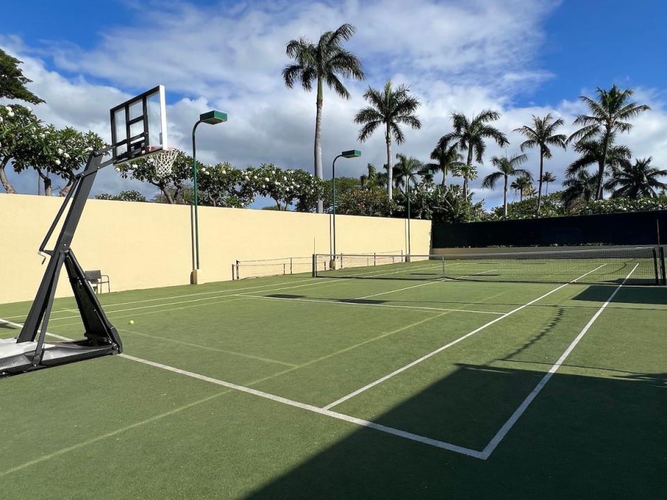 A tennis/pickleball court with a basketball hoop and fence at the Four Seasons Maui at Wailea.