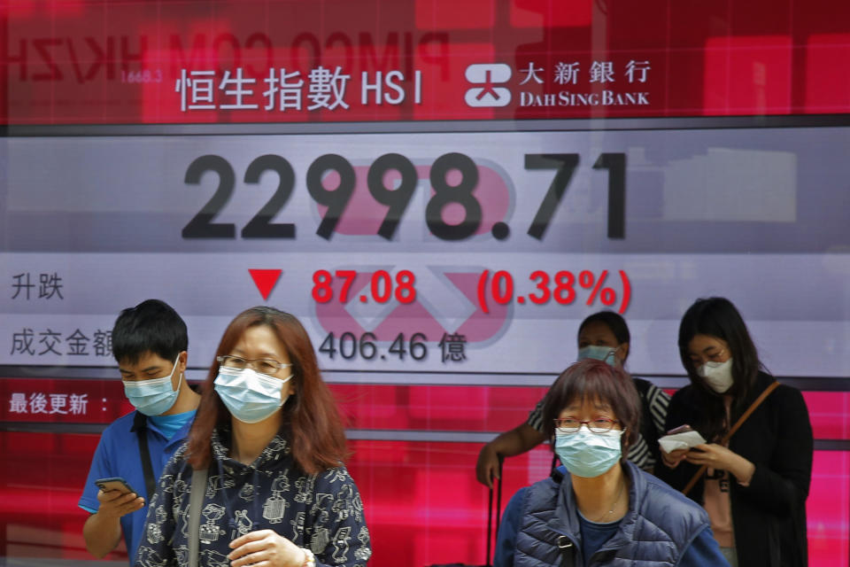 People walk past an electronic board showing Hong Kong share index outside a local bank in Hong Kong, Thursday, April 2, 2020. Asian stocks were meandering Thursday after a White House warning that as many as 240,000 Americans might die of the coronavirus sent Wall Street tumbling and signs of the outbreak's global economic cost increased.(AP Photo/Kin Cheung)