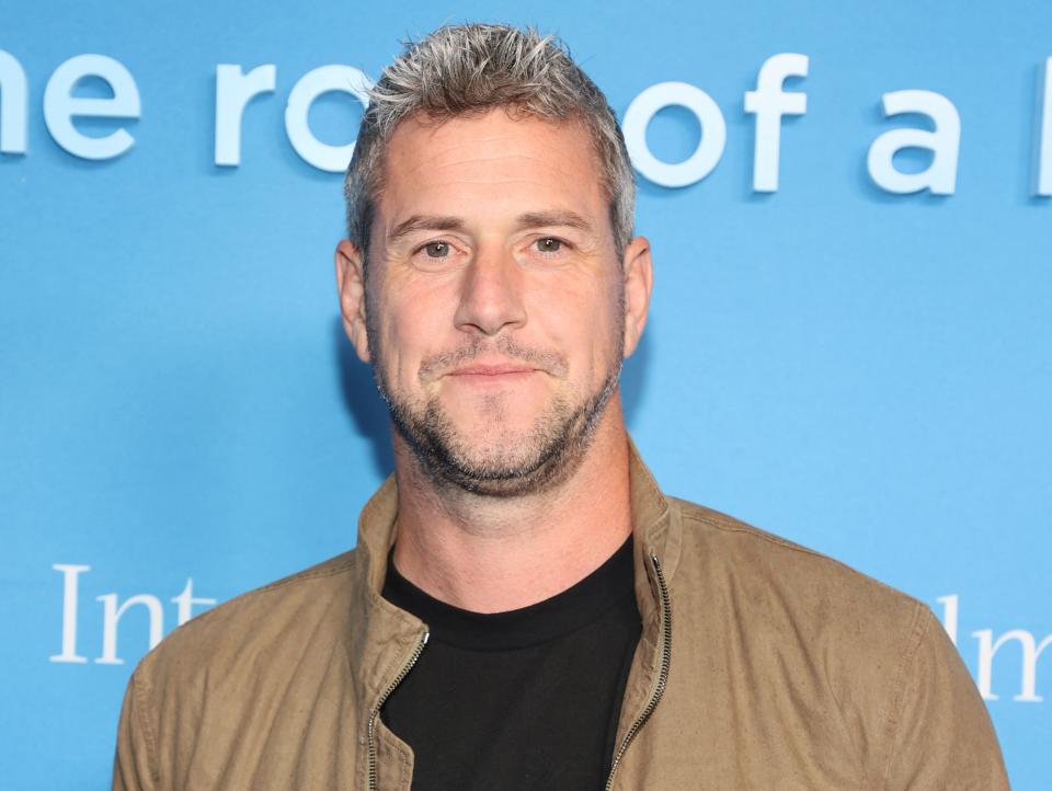 Ant Anstead smiles in front of a blue backdrop.