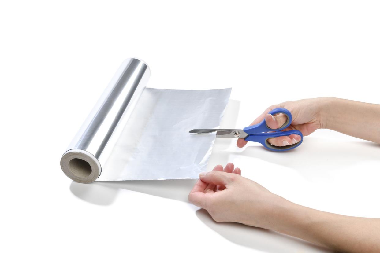 Lifehack; female hand cutting aluminum foil to sharpen scissors isolated on white background