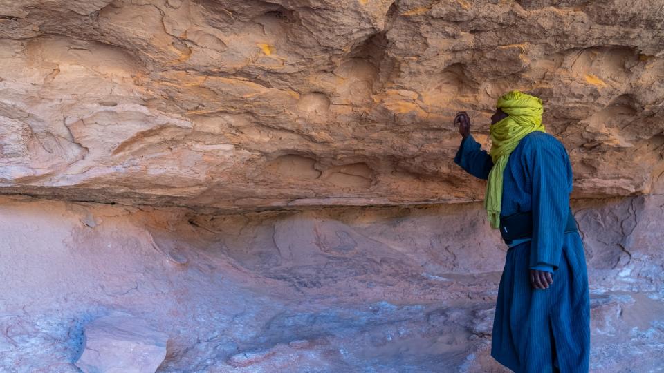 A touareg nomad standing next to an exposed sandstone wall in the desert