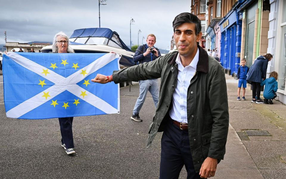 A nationalist demonstrator holds a flag as she welcomes Britain's Chancellor of the Exchequer Rishi Sunak to the Isle of Bute last month - Reuters