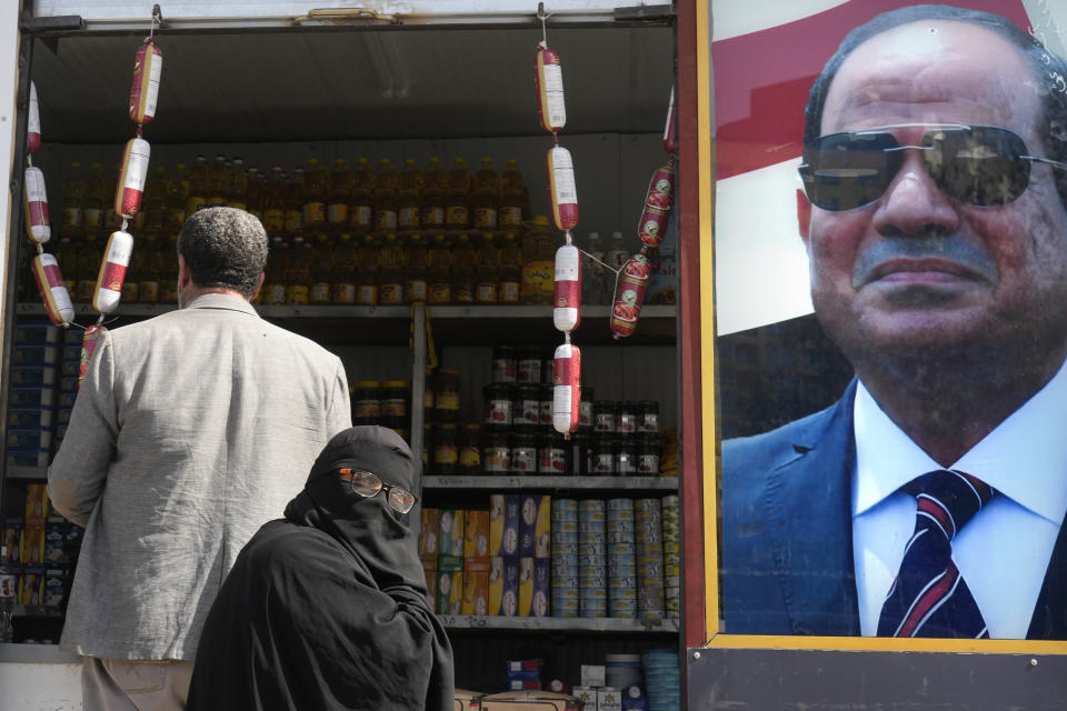 Clients buy groceries at a government sponsored shop fronted with Egyptian President Abdel Fattah el-Sissi poster in Cairo, Egypt, Monday, Feb. 27, 2023. Egypt is embarking on a privatization push to help its cash-strapped government, after pressure from the International Monetary Fund. The new policy is supposed to be a serious departure for the Egyptian state, which has long maintained a tight grip over sectors of the economy. (AP Photo)