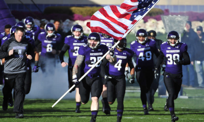 Northwestern football player leading his team onto the field while holding an American flag.