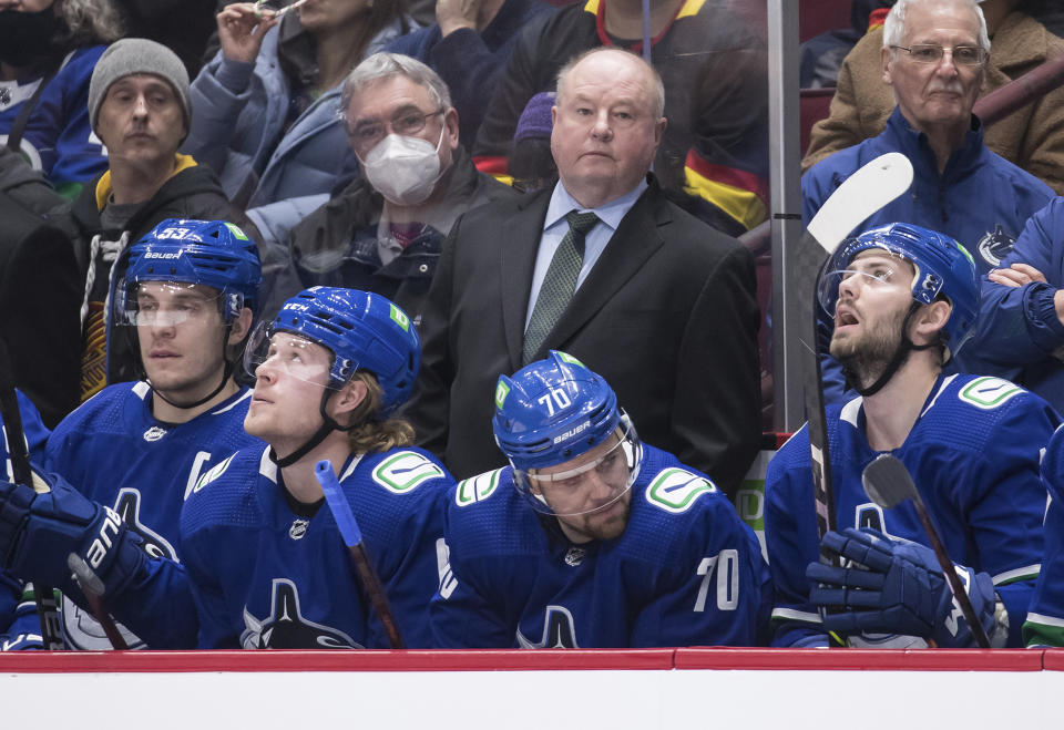 New Vancouver Canucks head coach Bruce Boudreau, center back, stands on the bench behind, from left to right, Bo Horvat, Brock Boeser, Tanner Pearson and Jason Dickinson during first-period NHL hockey game action against the Los Angeles Kings in Vancouver, British Columbia, Monday, Dec. 6, 2021. Darryl Dyck/The Canadian Press via AP)