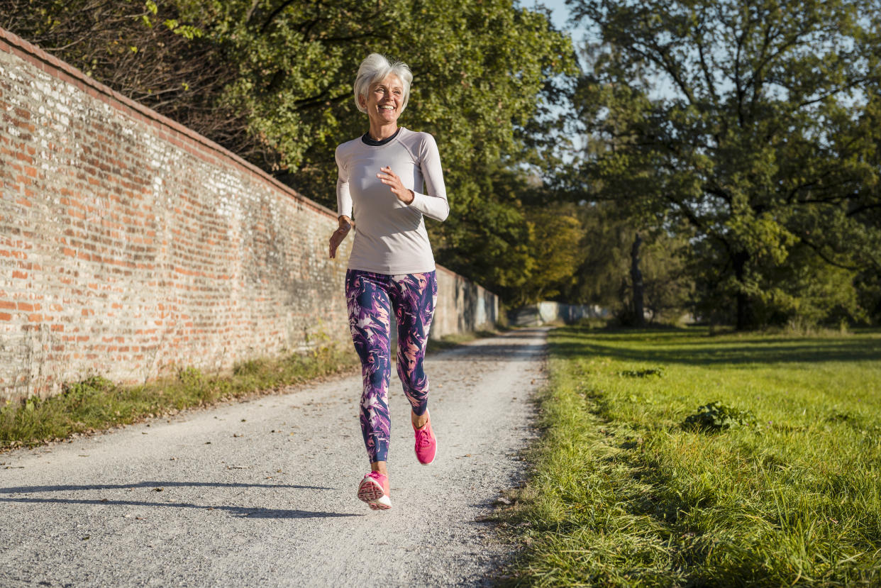 Senior woman running along brick wall in a park