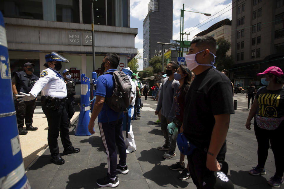 A Mexican police officer gives social-distancing and precautionary COVID-19 related guidelines to tourists in the historic center of Mexico City, Friday, July 3, 2020. Limited reopening of restaurants and other businesses in the capital this week came as new coronavirus cases continued to climb steadily. (AP Photo/Fernando Llano)