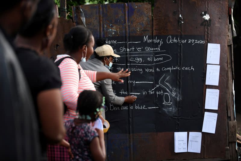 Educator Mckoy Phipps writes a lesson on a blackboard painted on a zinc fence during the coronavirus disease (COVID-19) outbreak in Kingston