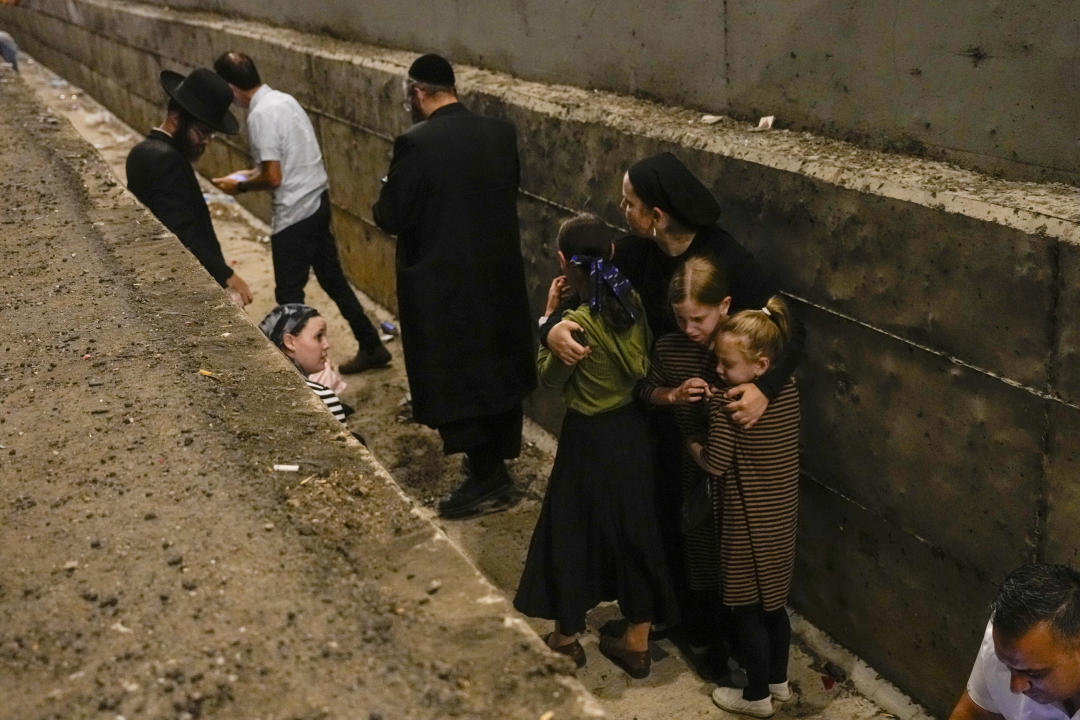 People take cover on the side of the road as a siren sounds a warning of incoming missiles fired from Iran on a freeway in Shoresh, between Jerusalem and Tel Aviv in Israel Tuesday, Oct. 1, 2024.(AP Photo/Ohad Zwigenberg)