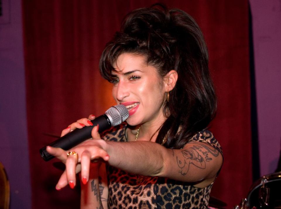 amy winehouse pointing out toward an audience as she holds a microphone and smiles while singing