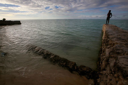 A boy stands on top of a seawall near the village of Tangintebu on South Tarawa in the central Pacific island nation of Kiribati May 26, 2013. REUTERS/David Gray/File Photo