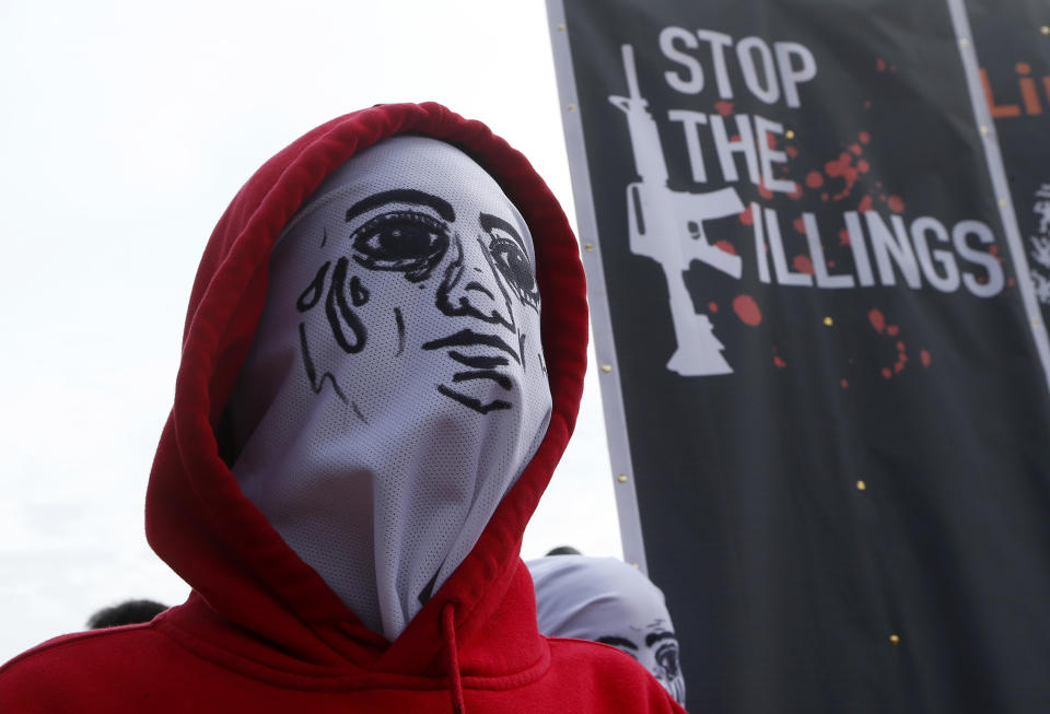 FILE - In this July 23, 2018 file photo, a masked demonstrator stands next to a banner protesting the thousands of victims of Philippine President Rodrigo Duterte's so-called war on drugs in Quezon, northeast of Manila, Philippines. Nearly 5,000 drug suspects, mostly from the ranks of the poor, have been killed so far in reported clashes with police, and more than 155,000 others arrested. Trump praised the campaign in a phone call with Dutarte, telling him, “What a great job you are doing,” according to a leaked transcript of the call. (AP Photo/Bullit Marquez, File)