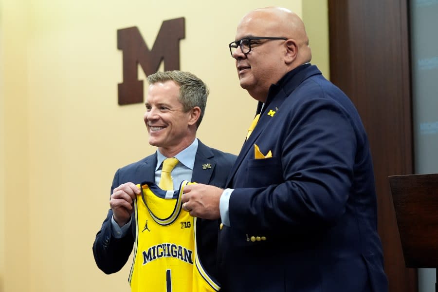 Dusty May, left, is presented a Michigan jersey by Athletic Director Warde Manuel before being introduced as the new Universtiy of Michigan NCAA college basketball head coach, Tuesday, March 26, 2024, in Ann Arbor, Mich. (AP Photo/Carlos Osorio)