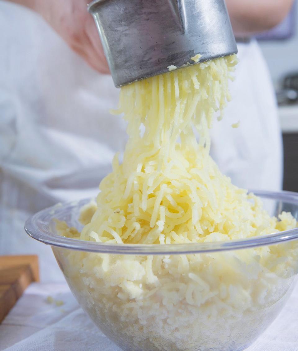 Cropped shot of woman using potato ricer in kitchen