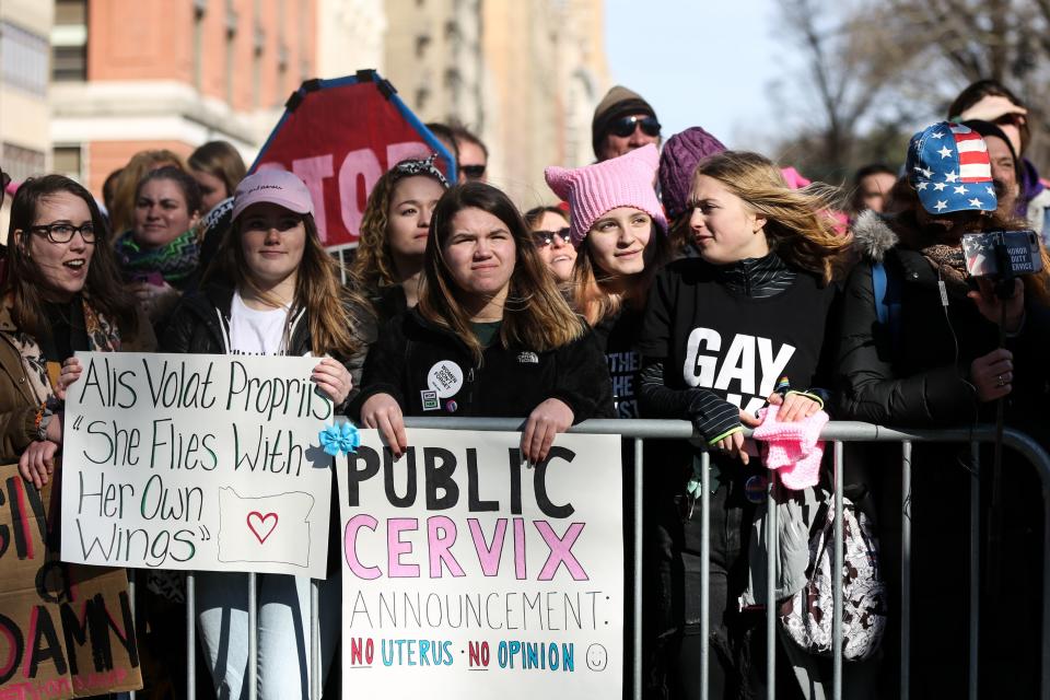 Women hold banners reading 'Alis Volat Propriis : She Flies With Her Own Wings.