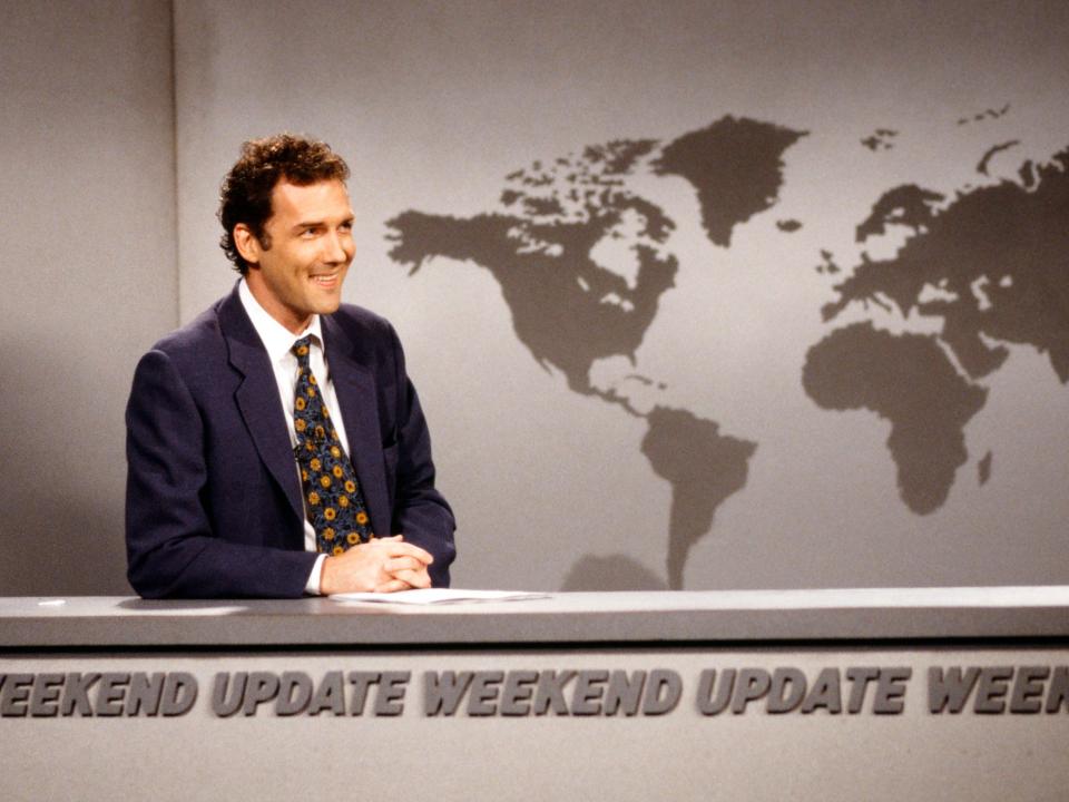 Norm Macdonald sitting at Weekend Update dask