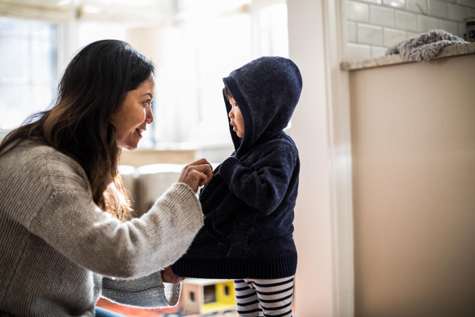 Mother helping daughter (2yrs) put on coat