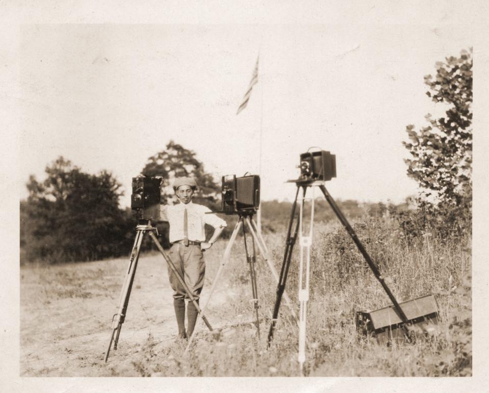 George Masa poses in field with three view cameras on tripods circa 1920-30.