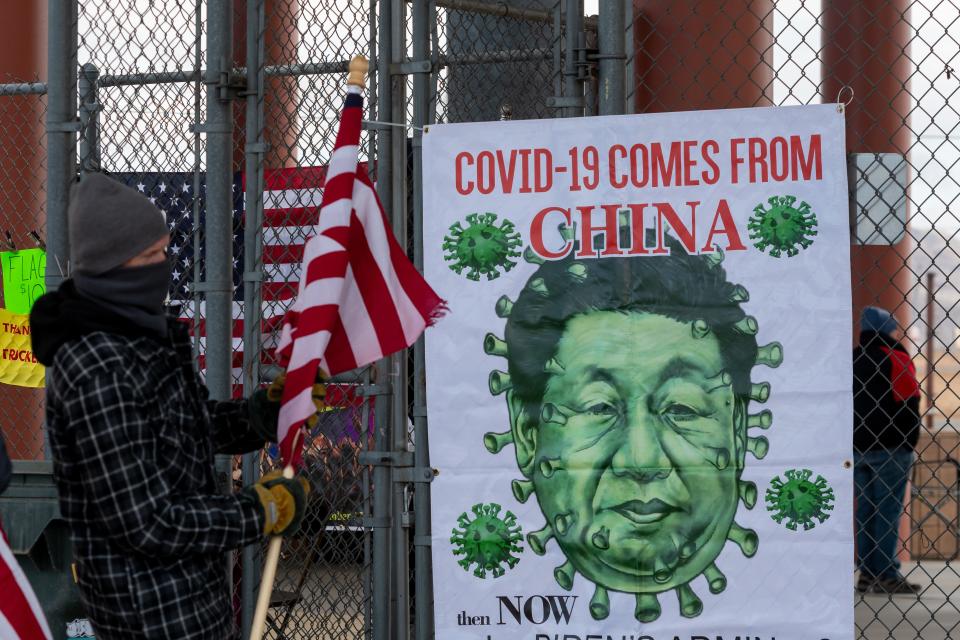 An attendee stands next to a sign at the People's Convoy rally, a movement opposing COVID-19 mandates, in Adelanto Stadium in Adelanto on Wednesday, Feb. 23, 2022.