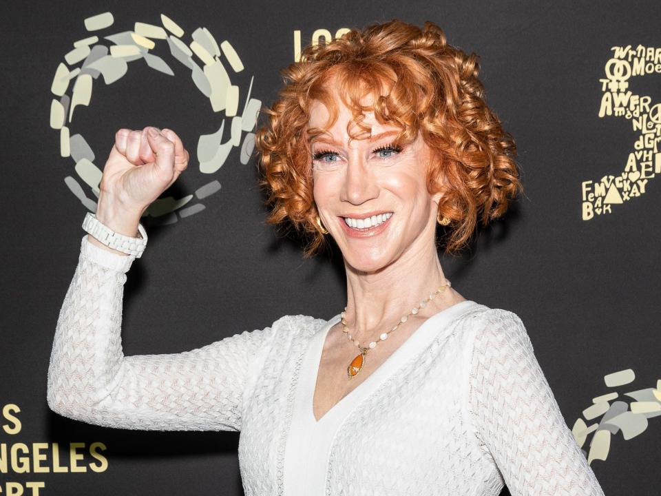 Kathy with red curly hair smiling with her first in the air.