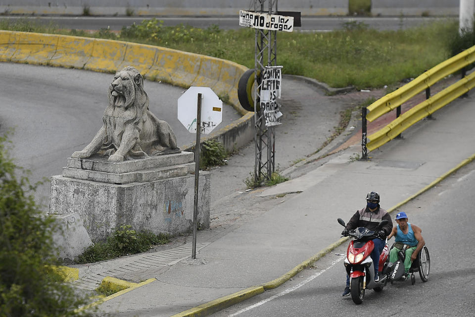 Manuel Mendoza viaja en su silla de ruedas agarrándose a la parte trasera de una motocicleta en el barrio La Paz de Caracas, Venezuela, el sábado 14 de noviembre de 2020. (AP Foto/Matias Delacroix)