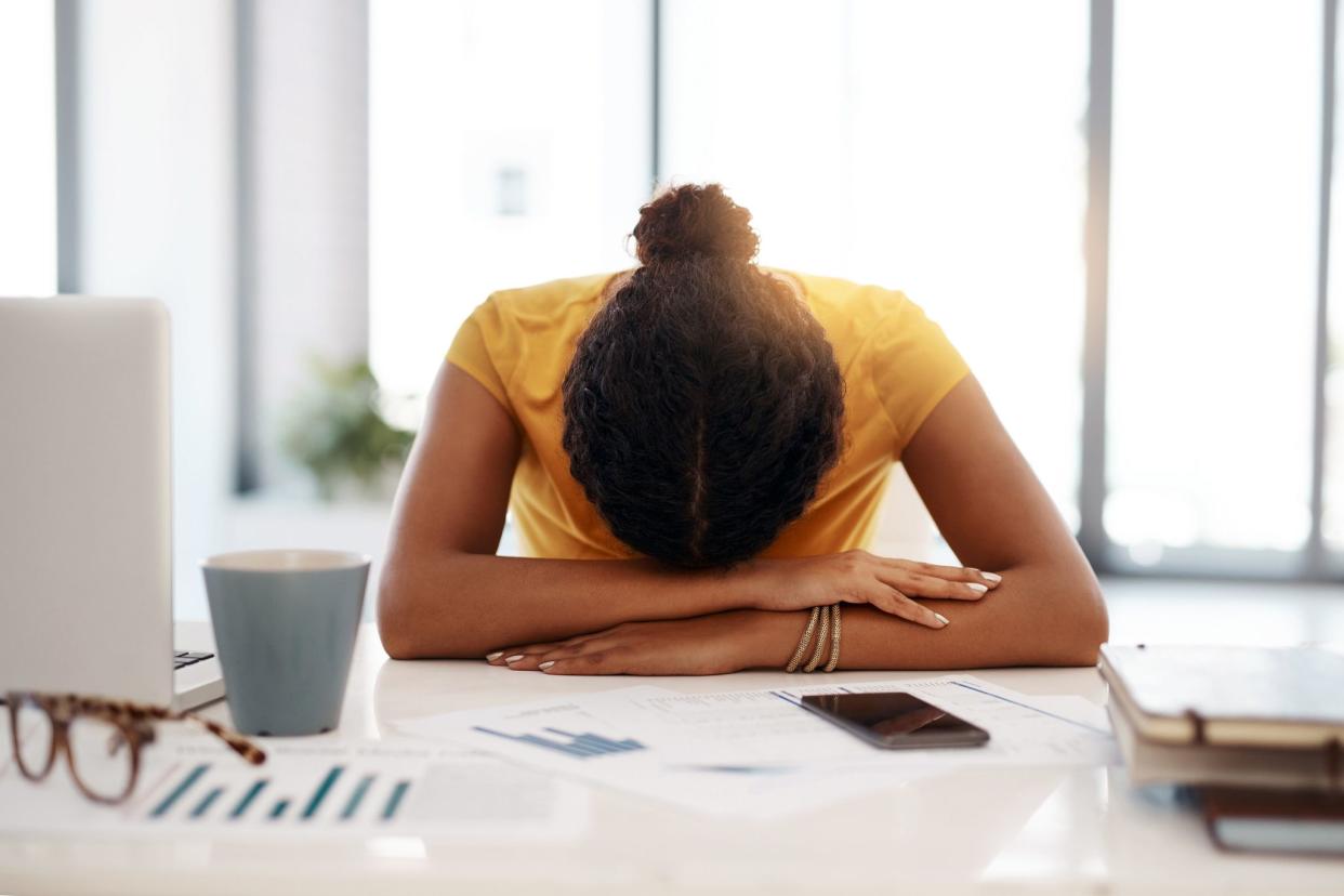 woman with head and forearms resting on desk, exhausted, in office