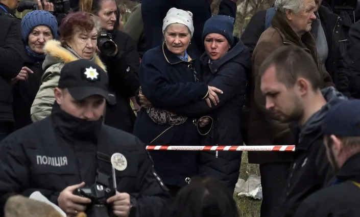 Семьи собираются, чтобы опознать своих близких, пока следователи по военным преступлениям фотографируют трупы, найденные в братской могиле в Буче.