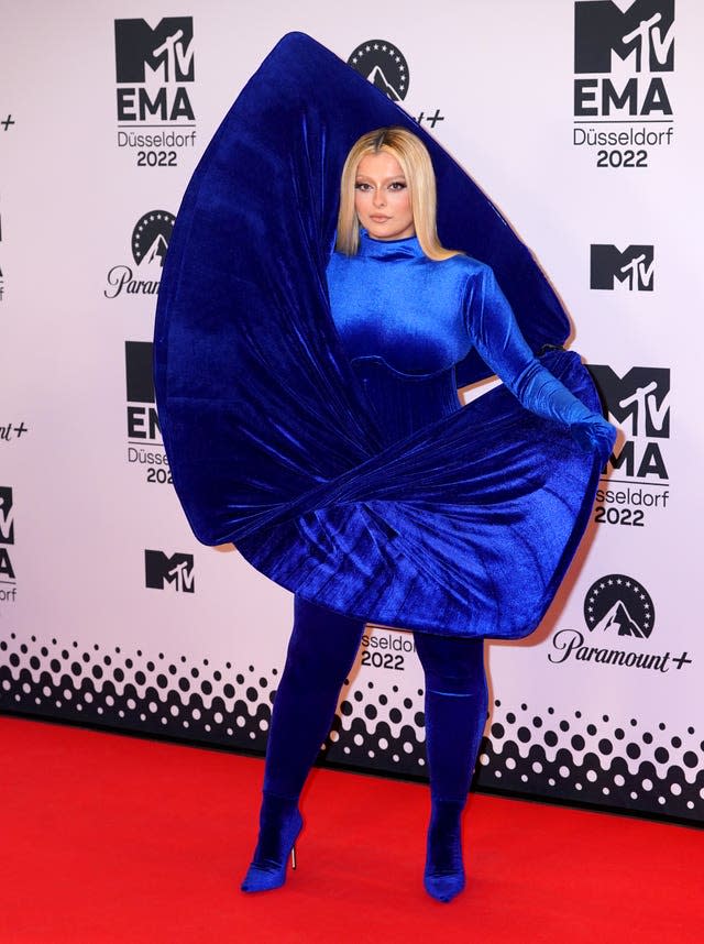 Bebe Rexha posing on red carpet, wearing a blue dress with rises above her head