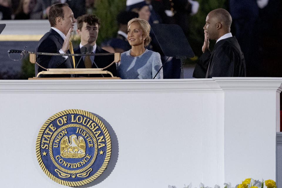 Louisiana Republican Gov. Jeff Landry, left, stands with his wife Sharon Landry, center right, and son J.T. Landry, center left, as he is sworn in by former district Judge Roger Hamilton, right, at an inauguration ceremony at the State Capitol building in Baton Rouge, La., Sunday, Jan. 7, 2024. The ceremony was moved because of forecasted rain on Monday, Jan. 8, the actual date Landry officially becomes governor. (AP Photo/Matthew Hinton)