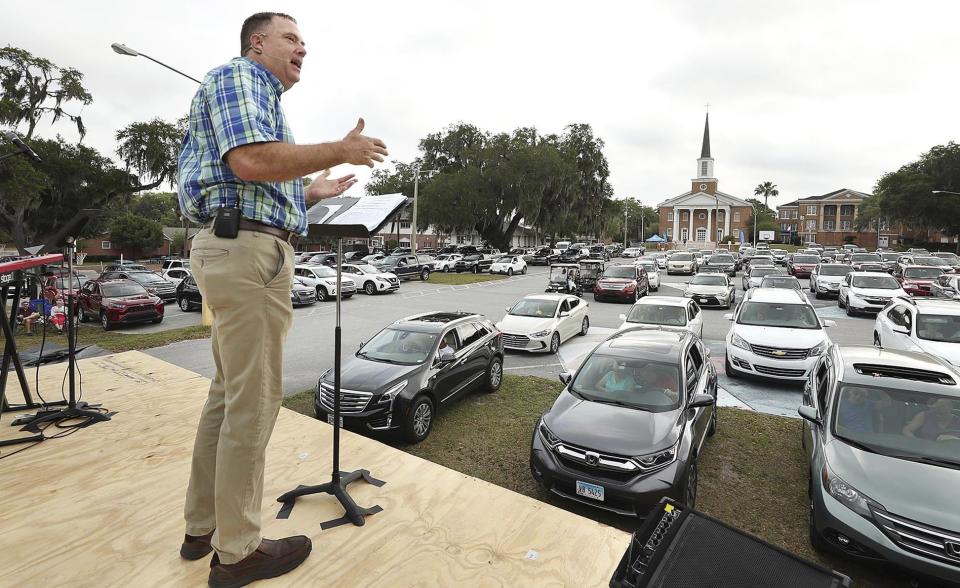 Pastor Cliff Lea preaches over a parking lot filled with cars during a drive-in service at the First Baptist Church of Leesburg on Easter Sunday, April 12, 2020. With coronavirus prevention measures shuttering houses of worship, pastors across the country are urging parishioners to use their cars to safely bring their communities closer together. Drive-in churches are popping up so worshipers can assemble. (Stephen M. Dowell/Orlando Sentinel via AP)