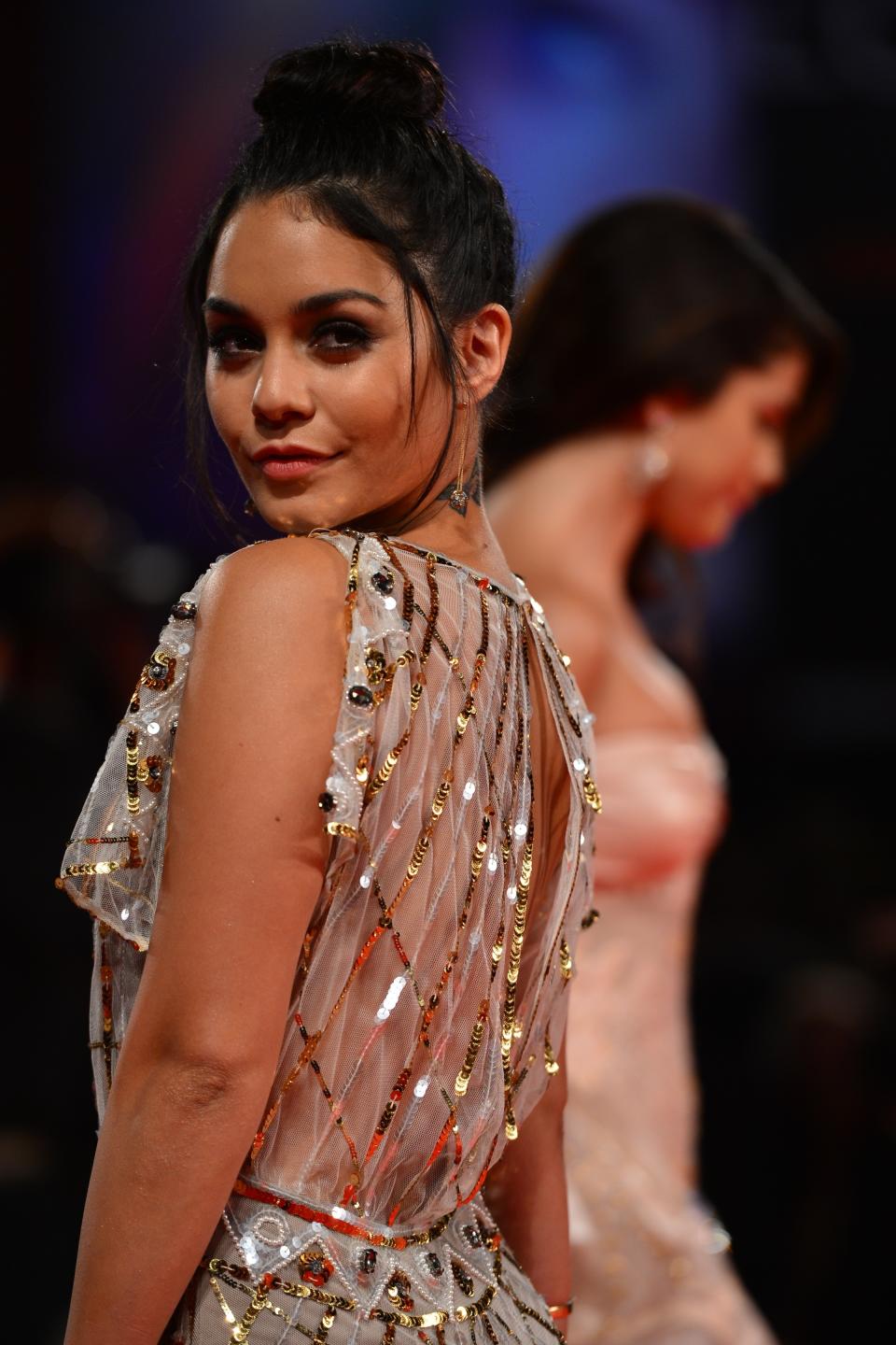 Vanessa Hudgens in a sequined, sheer dress on the red carpet, with another person slightly out of focus in the background
