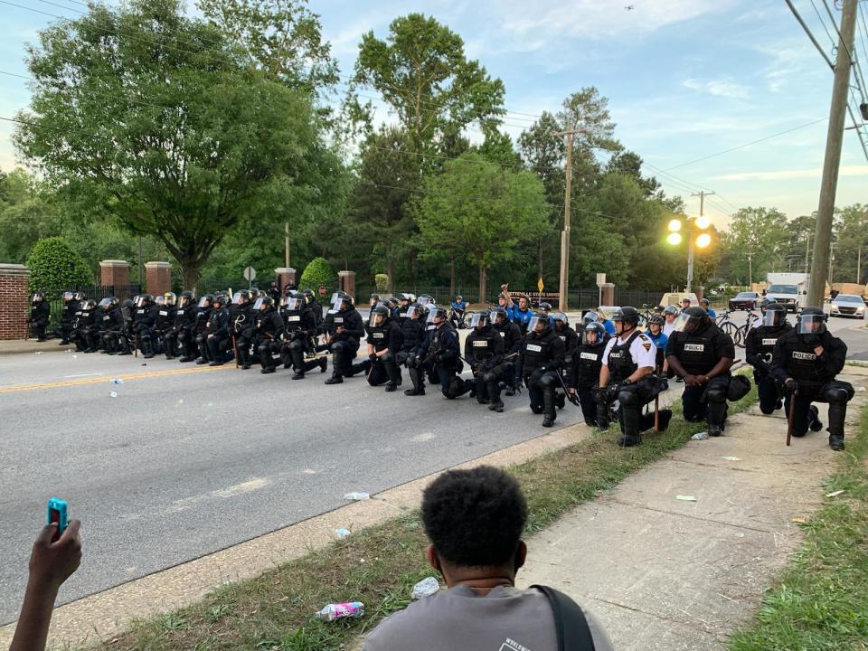 Fayetteville police officers in riot gear take a knee during a protest in Fayetteville on Monday.