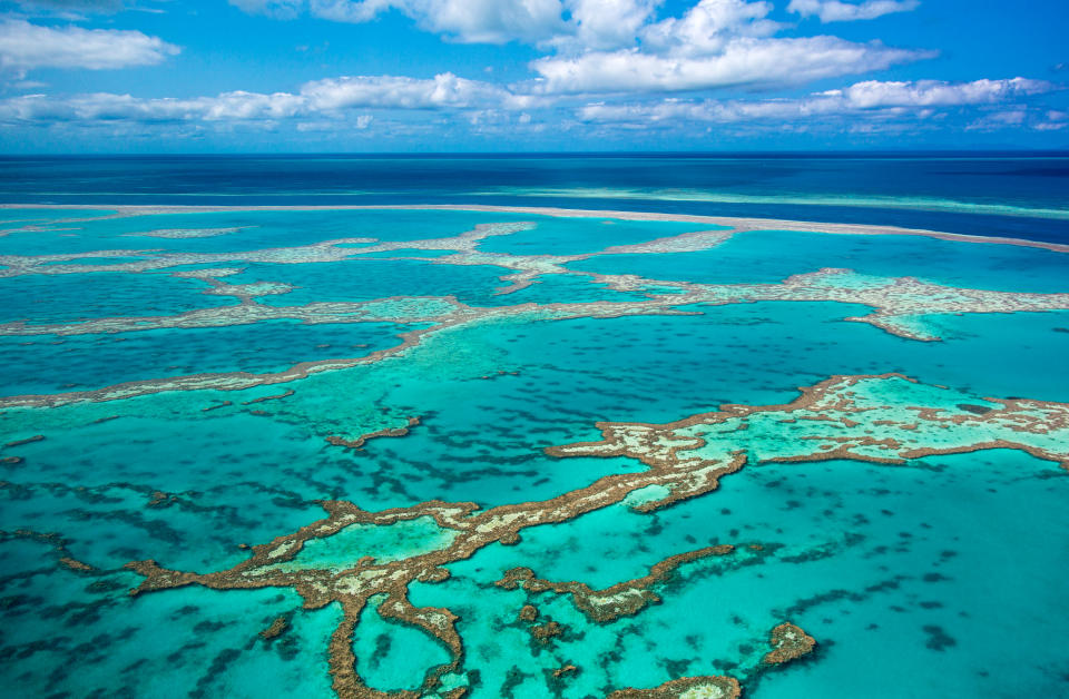 Aerial photo of Great barrier reef showing reef area with some blue water and slightly cloudy sky in background.