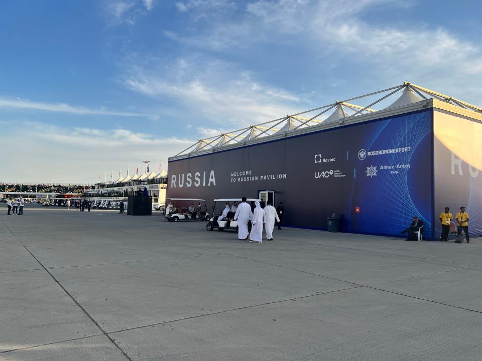 The Russian Pavilion at the Dubai Airshow, a large windowless chalet, with the viewing stand in the background and men wearing white kandurahs in the foreground.