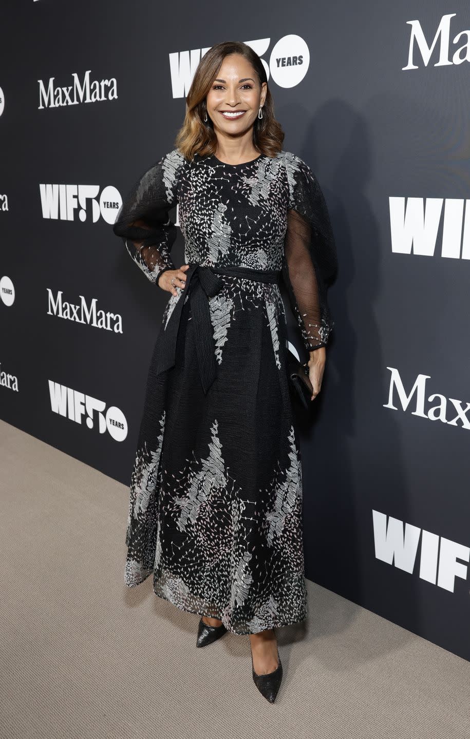 salli richardson whitfield, a woman wearing a patterned black and gray dress and burgundy lipstick, posing for the camera with her hand on her hip