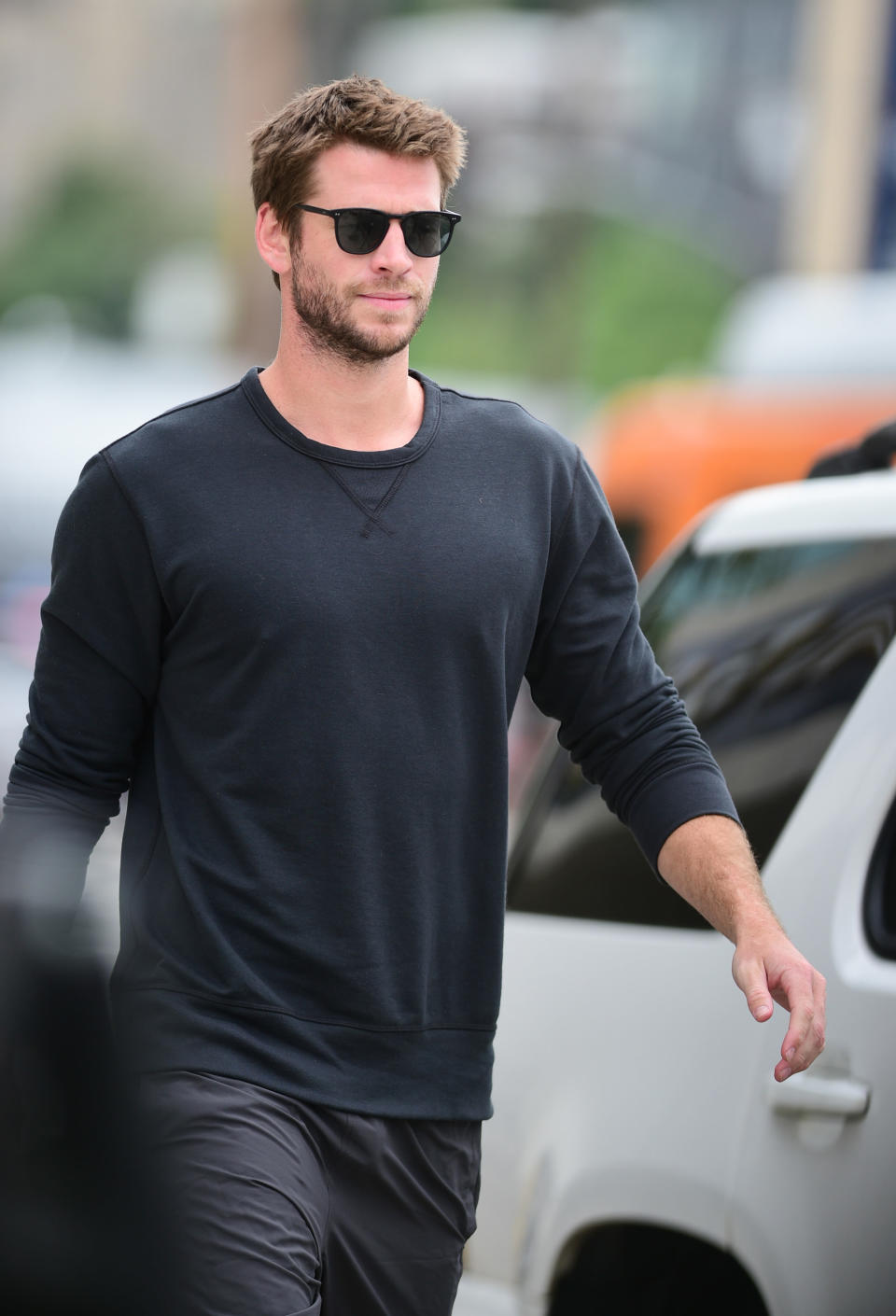 A photo of Liam Hemsworth wearing a black long-sleeve shirt, black jeans and sunglasses.