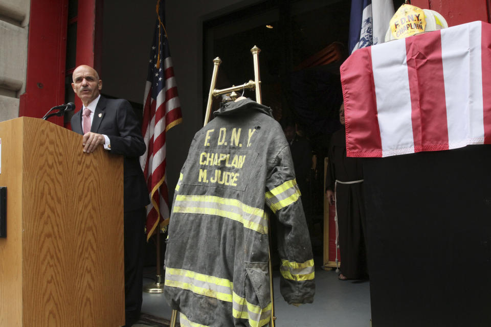 FILE - In this Sunday Sept. 11, 2011 file photo, the bunker coat and helmet worn by FDNY Chaplain Mychal Judge are displayed as City of New York Fire Commissioner Salvatore J. Cassano speaks at the New York City Fire Museum in New York during a memorial ceremony for the 343 members of the FDNY who lost their lives in the World Trade Center attacks. The bunker coat and helmet worn by Father Judge on Sept. 11, 2001, were dedicated to the museum during the service. (AP Photo/Tina Fineberg, File)