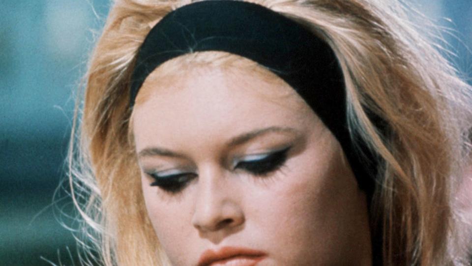 French actress Brigitte Bardot on the set wearing a thick black headband and blue eye makeup 