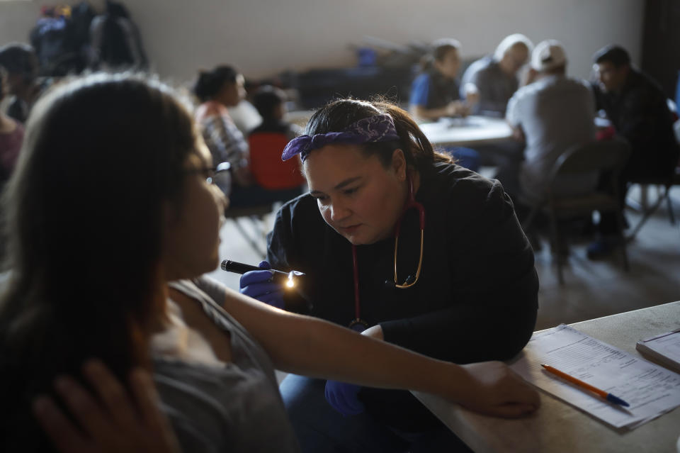In this Dec. 14, 2019, photo, Dr. Psyche Calderon works with a patient in a shelter for migrants in Tijuana, Mexico. Calderon is a general practitioner volunteering her time to provide care for Central Americans stuck in Mexico while they try to obtain asylum in the United States. (AP Photo/Gregory Bull)