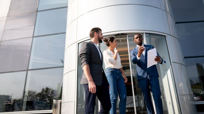 Portrait of a happy salesman selling a car to a couple at the dealership â€“ lifestyle concepts.