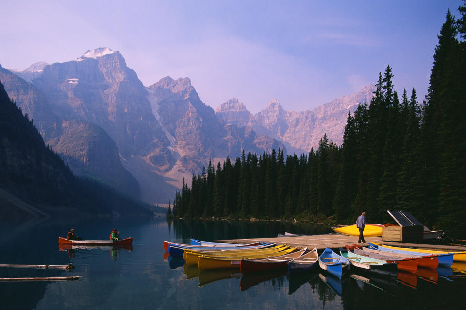 Canoes at a mountain lake with a person standing on the dock and two people in a canoe