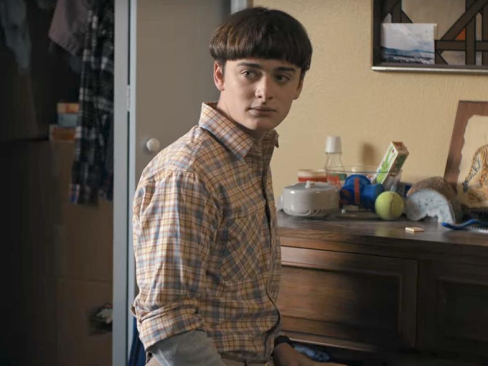 A teenage boy kneeling on the ground in front of a dresser.