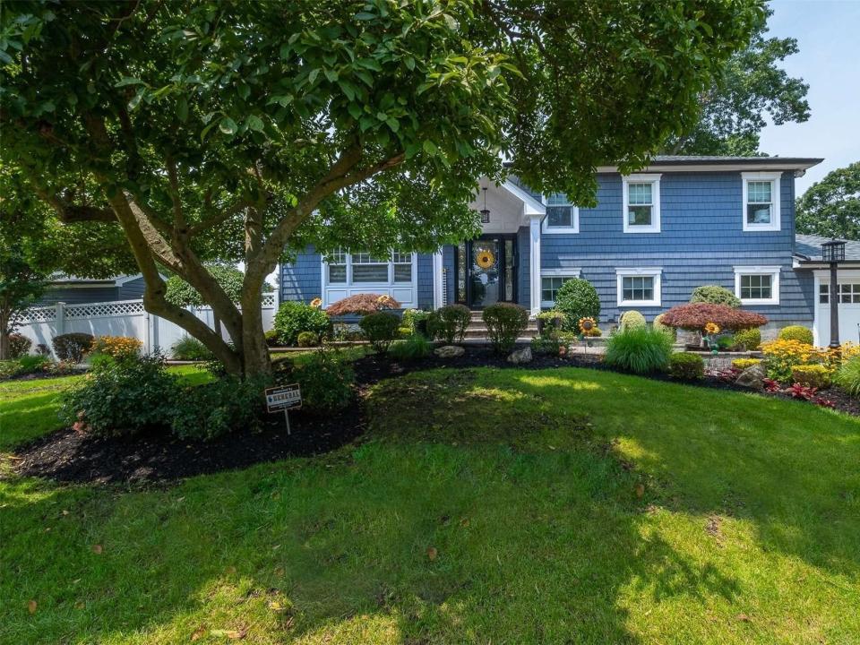 The exterior of the blue house for sale in long island covered by a tree