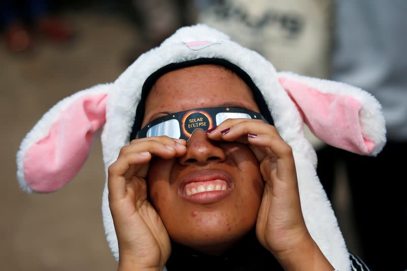 A girl wearing special protective glasses reacts as she observes the annular solar eclipse in Siak