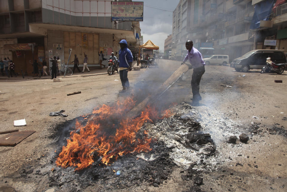 Ugandan plain-clothes security forces attempt to extinguish a burning barricade lit by protesters in a street in Kampala, Uganda, Monday, Aug. 20, 2018. Ugandan police fired bullets and tear gas to disperse a crowd of protesters demanding the release of jailed lawmaker, pop star, and government critic Kyagulanyi Ssentamu, whose stage name is Bobi Wine. (AP Photo/Stephen Wandera)