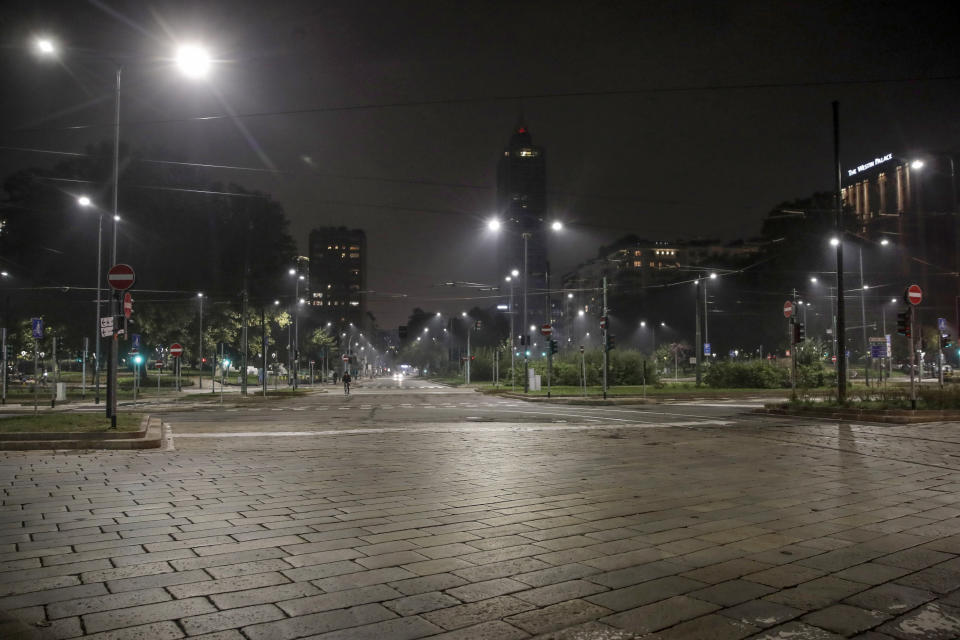 An empty street is lit by street lights in Milan, northern Italy, Sunday, Oct. 25, 2020. Since the 11 p.m.-5 a.m. curfew took effect last Thursday, people can only move around during those hours for reasons of work, health or necessity. (AP Photo/Luca Bruno)