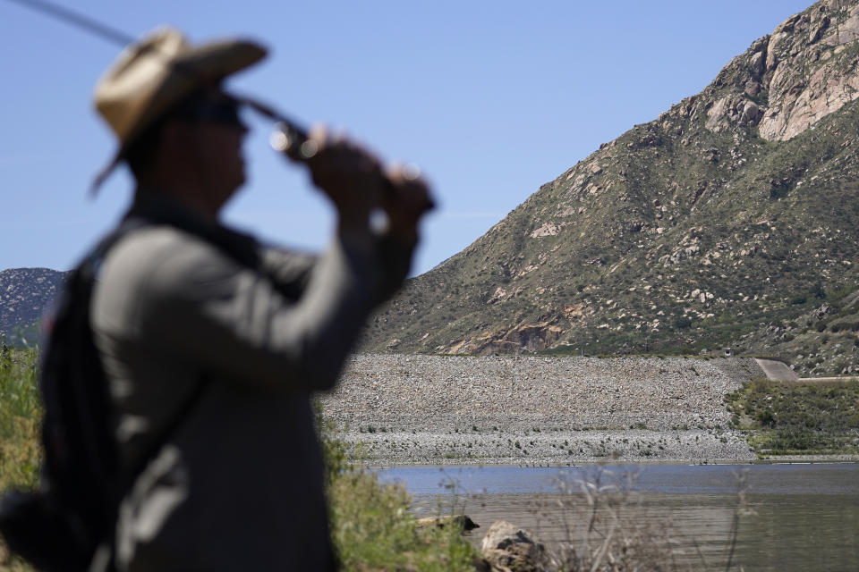 Samuel Santos casts into El Capitan Reservoir as he fishes near the dam, seen in background, Friday, April 8, 2022, in Lakeside, Calif. Constructed four generations ago, the massive rock and clay dam at El Capitan Reservoir is capable of storing over 36 billion gallons of water — enough to supply every resident in San Diego for most of a year. Today, it's three-quarters empty — intentionally kept low because of concerns it could fail under the strain of too much water. (AP Photo/Gregory Bull)