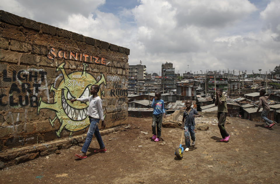FILE - In this April 22, 2020, file photo, children walk past an informational mural depicting the coronavirus and warning people to sanitize to prevent its spread, painted by graffiti artists from the Mathare Roots youth group, in the Mathare informal settlement, of Nairobi, Kenya. The options for African students eager to keep studying while schools remain closed because of the coronavirus pandemic seems varied, but the reality for many is that they will fall behind and possibly drop out of school forever, worsening inequality on an already unequal continent. (AP Photo/Brian Inganga, File)